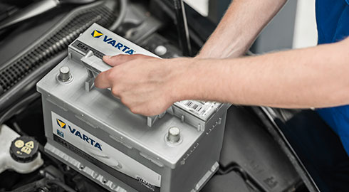 A man puts down a battery into a car- only his arms are displayed.