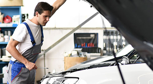 Een blije man die lachend voor een blauwe auto in een garage staat